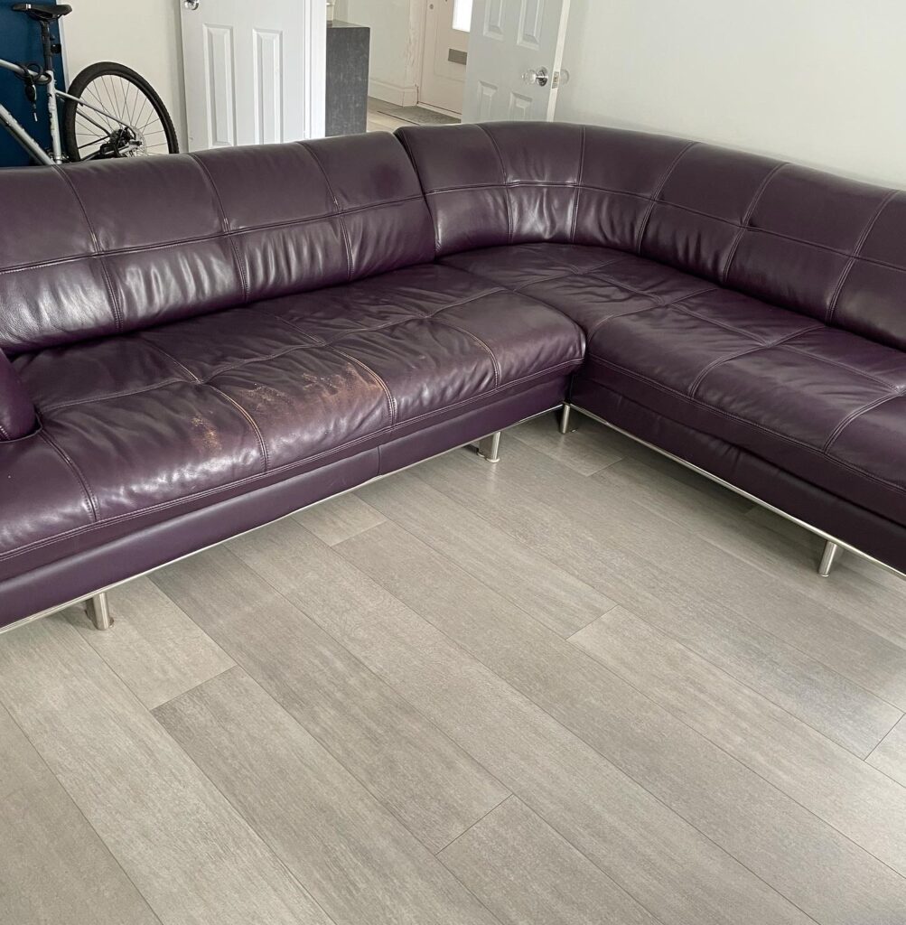 Plum-coloured leather corner sofa showing worn and faded seat cushions prior to professional leather restoration.
