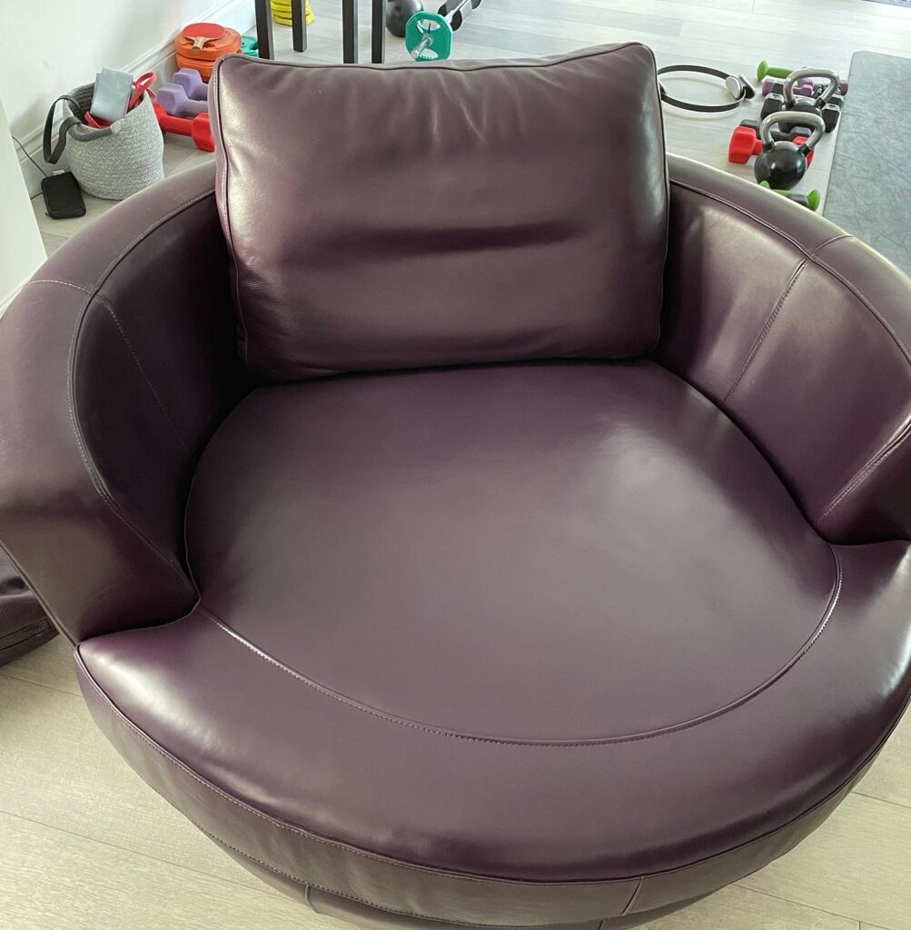 Round plum leather swivel chair professionally restored with refreshed upholstery and a smooth leather surface.