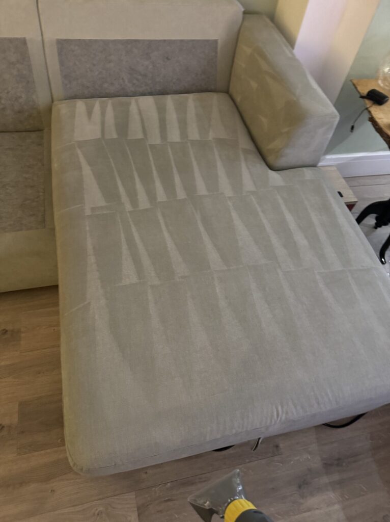 Curved fabric ottoman showing professional upholstery cleaning results with visible cleaning patterns across the surface.