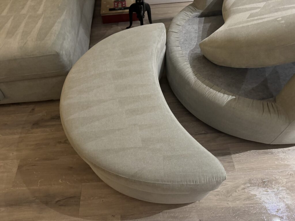 Curved fabric ottoman showing professional upholstery cleaning results with visible cleaning patterns across the surface.