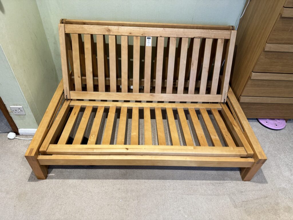Wooden sofa bed frame with slatted base and folded backrest, shown during furniture repair and restoration.
