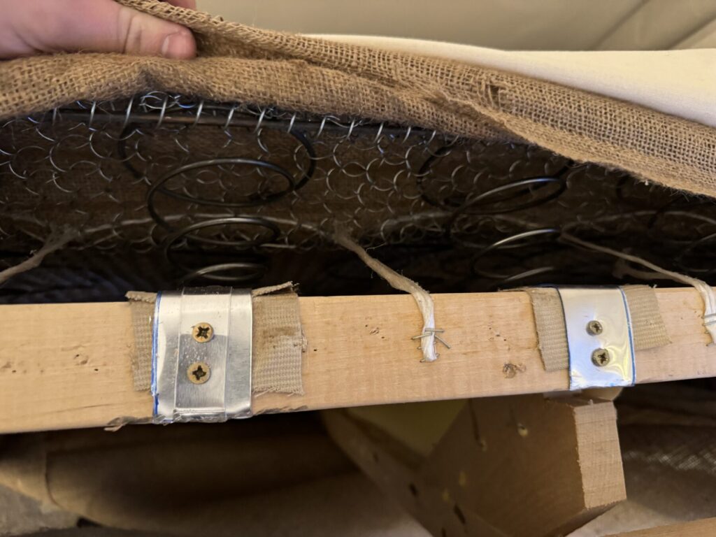 Close-up of a sofa frame with repaired springs and support webbing during professional upholstery and structural restoration.