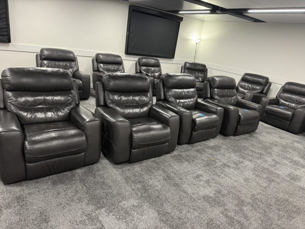 Home cinema room fitted with multiple black leather recliner chairs arranged in rows for luxury viewing.
