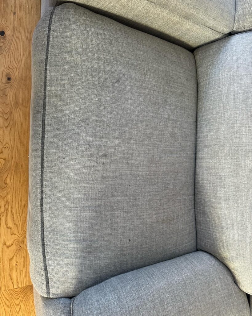 Light grey fabric sofa cushion showing multiple stains and marks prior to professional upholstery cleaning.