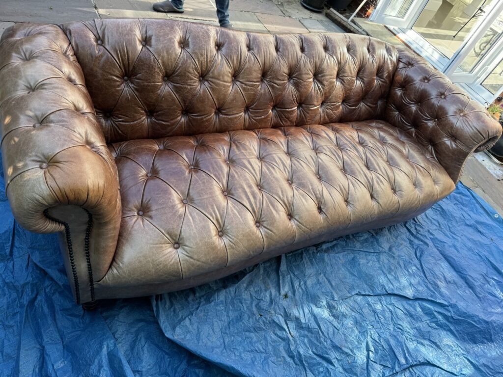 Brown Chesterfield leather sofa before being professionally restored with leather and traditional deep button-tufted upholstery.
