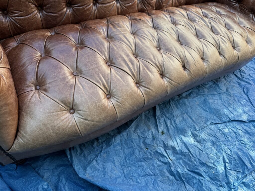 Close up of Brown Chesterfield leather sofa before being professionally restored with leather and traditional deep button-tufted upholstery.