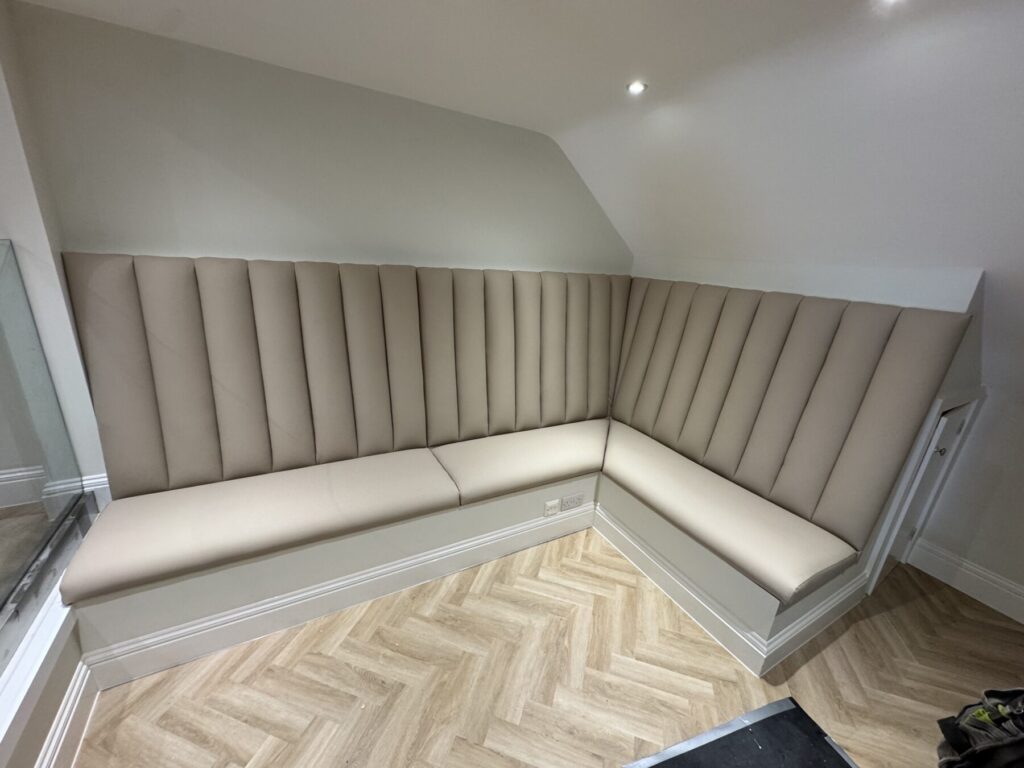 Custom upholstered corner banquette seating with vertical panel detailing and a soft beige fabric finish.
