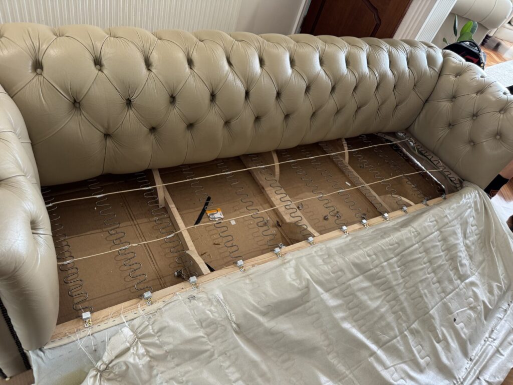 Cream Chesterfield leather sofa with seat cushion removed, exposing the internal spring system during furniture repair.