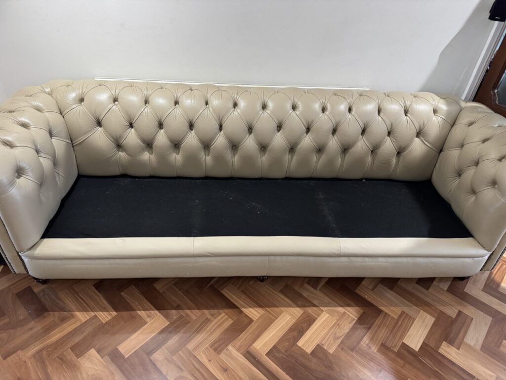 Cream Chesterfield leather sofa with seat cushions removed, exposing the frame during upholstery repair and restoration.
