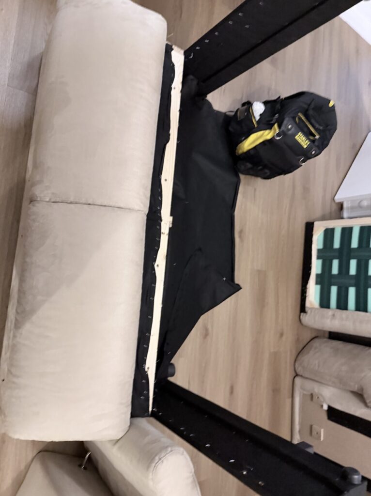 Upholstered sofa turned upside down during structural frame repair and furniture restoration work.