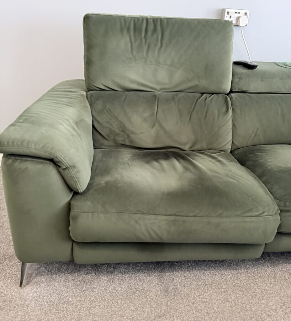 Green fabric corner sofa showing signs of wear and cushion flattening prior to professional restoration.