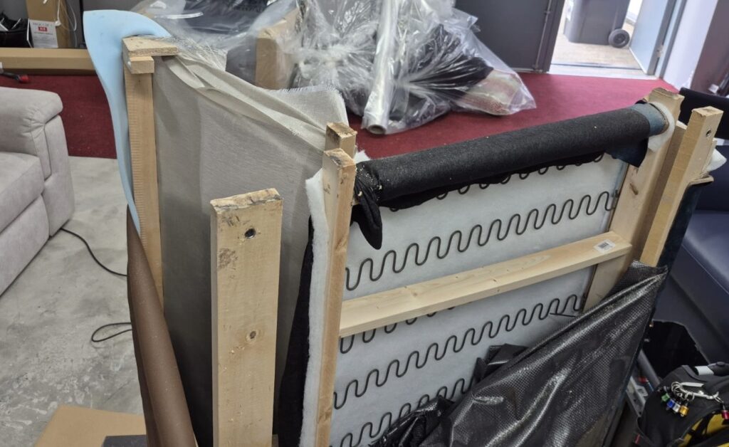 Exposed sofa frame and spring system undergoing structural repair and reinforcement in a furniture workshop.