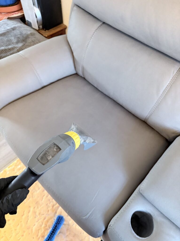 Professional extraction cleaning being carried out on a light grey fabric recliner chair.