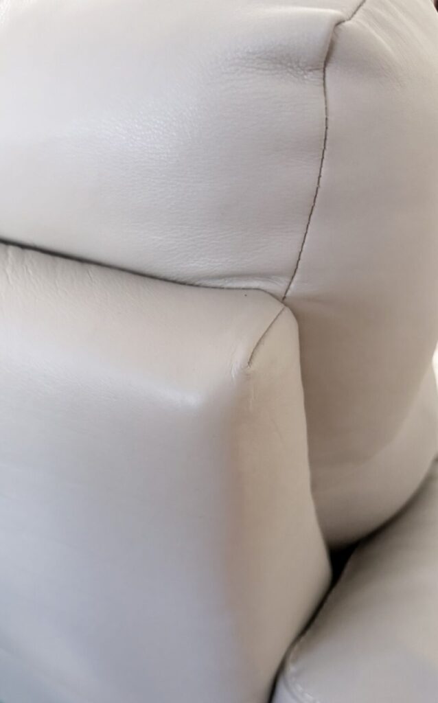 White leather sofa side panel showing a tear and surface damage prior to leather restoration.