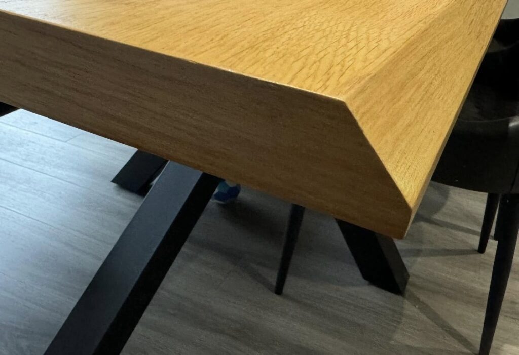 Close-up of a wooden dining table corner showing professional furniture repair and refinishing work.